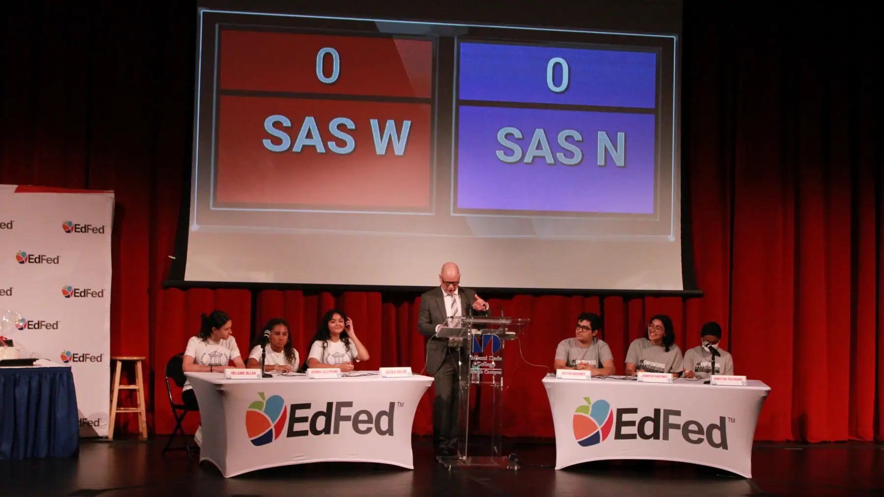 Two school teams face each other under a live scoreboard.