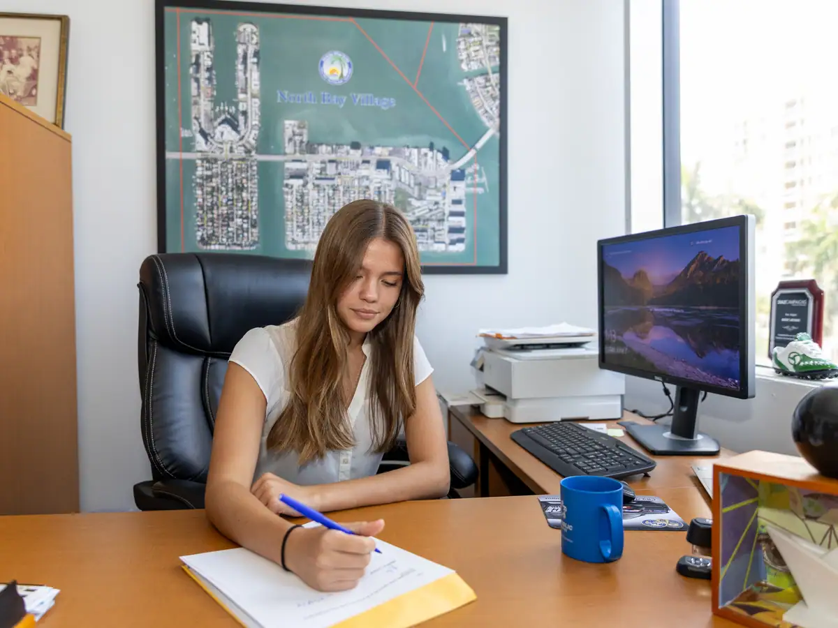 A student works from a municipal office desk, city planning map on the wall.